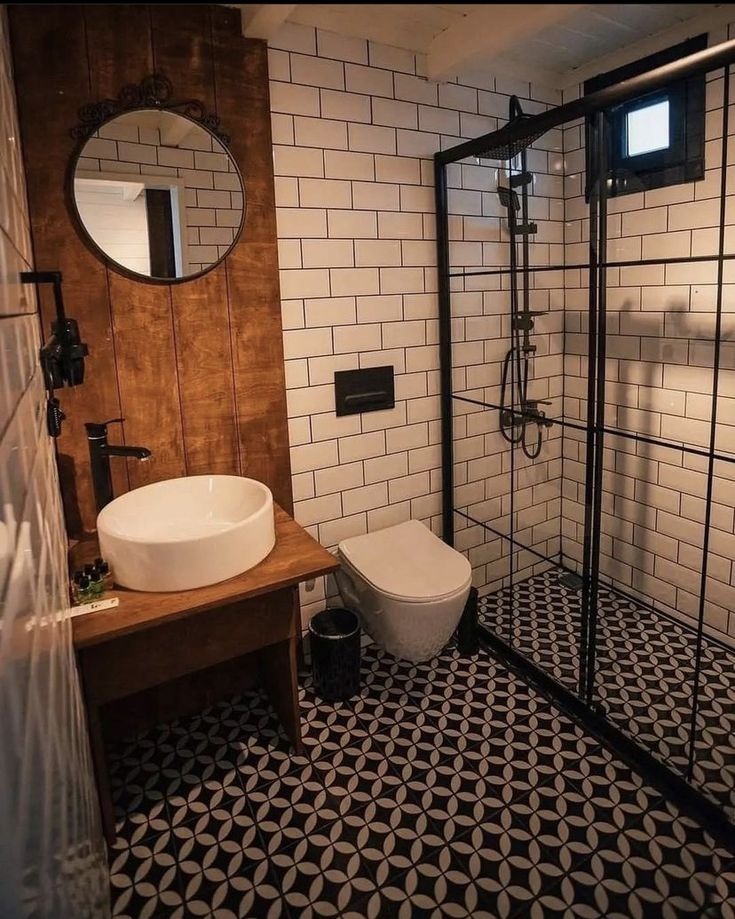 Nowoczesna łazienka z kabiną prysznicową typu walk-in, umywalką nablatową na drewnianym blacie, okrągłym lustrem z ozdobną ramą i biało-czarną mozaiką na podłodze.
