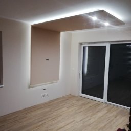 USŁUGI REMONTOWO-WYKOŃCZENIOWE MIKOŁAJ ŁUKOWIAK - Nowoczesny salon z podwieszanym sufitem z oświetleniem LED, drewnianą podłogą i dużymi przesuwnymi drzwiami balkonowymi.