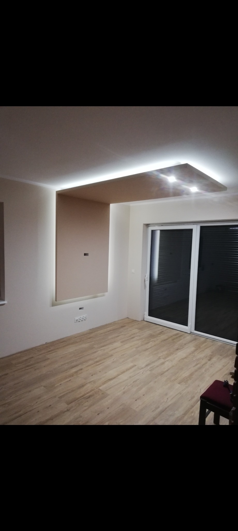 Nowoczesny salon z podwieszanym sufitem z oświetleniem LED, drewnianą podłogą i dużymi przesuwnymi drzwiami balkonowymi.