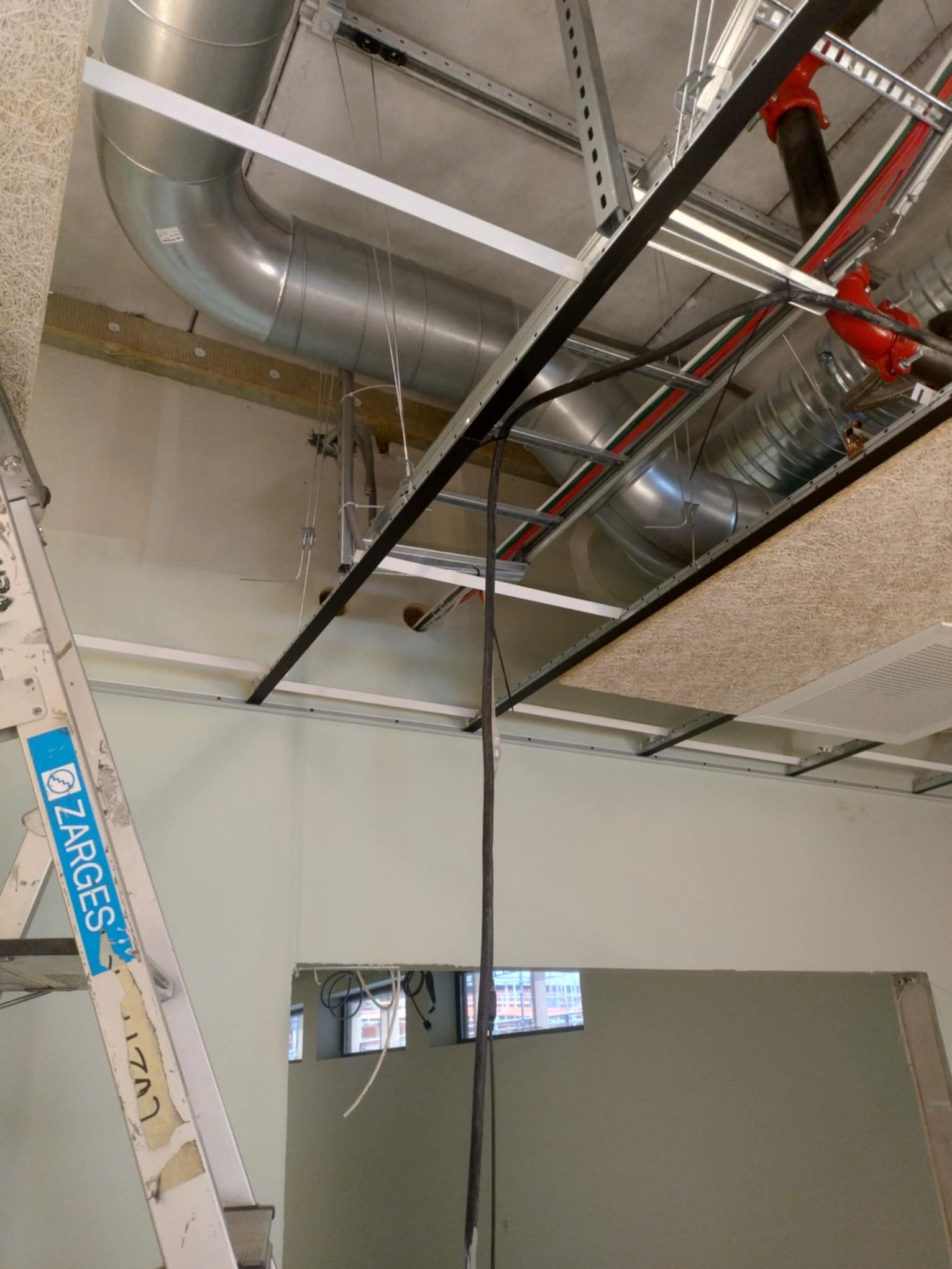 Szczegółowy widok instalacji wentylacyjnej z rurami z ocynkowanej blachy, elementami mocującymi i przewodami, zamontowanej pod sufitem w budynku w trakcie prac wykończeniowych, z widoczną drabiną...