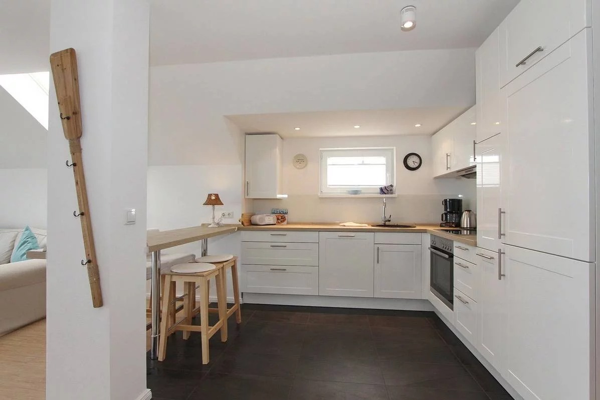 Jasna kuchnia z białymi szafkami, drewnianym blatem, ciemną podłogą i dekoracyjnym wiosłem z haczykami na ścianie.