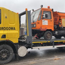 Firma Handlowo Usługowa Jarosław JANIK - Żółta laweta z napisem 'POMOC DROGOWA' przewozi pomarańczowy pojazd Multicar z posypywarką do soli, widoczne logo FCC.