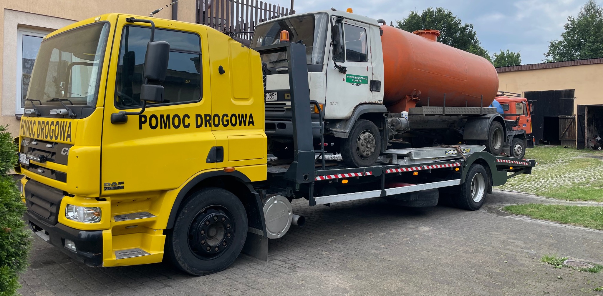 Żółta laweta DAF z napisem 'POMOC DROGOWA' przewozi białą ciężarówkę z pomarańczowym zbiornikiem na płyny.
