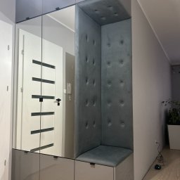 Rafał Bojek - Szara zabudowa przedpokoju z lustrami, siedziskiem obitym welurem i panelem ściennym z guzikami.