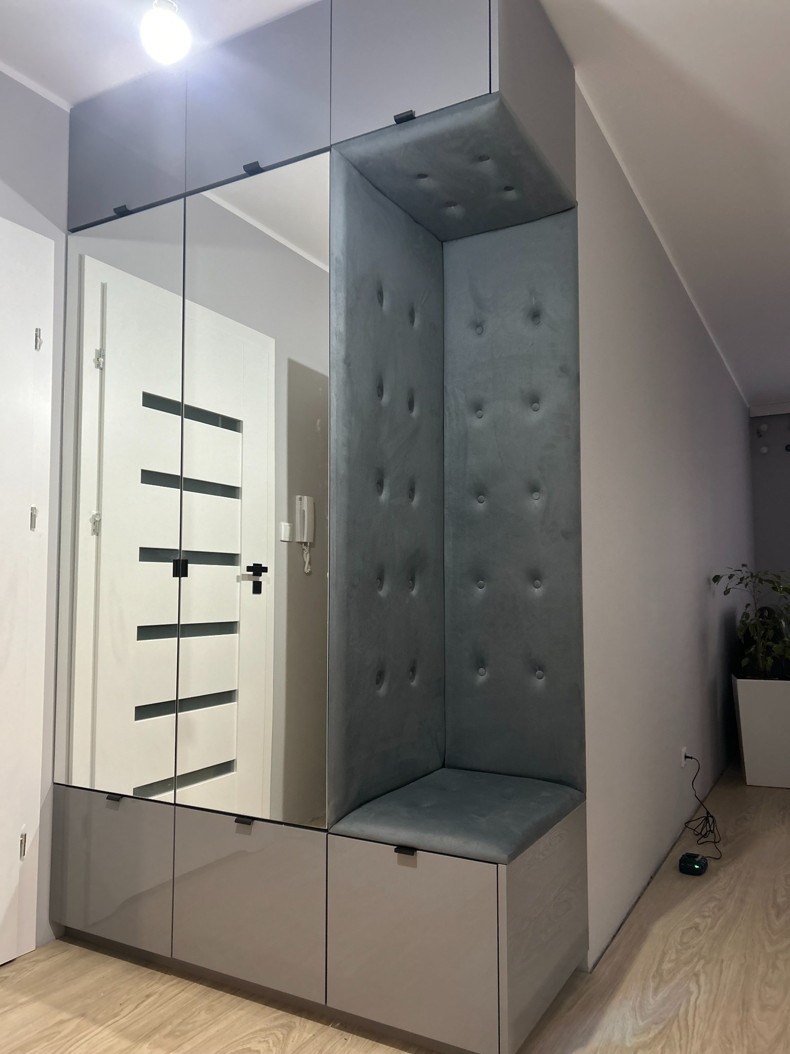 Szara zabudowa przedpokoju z lustrami, siedziskiem obitym welurem i panelem ściennym z guzikami.