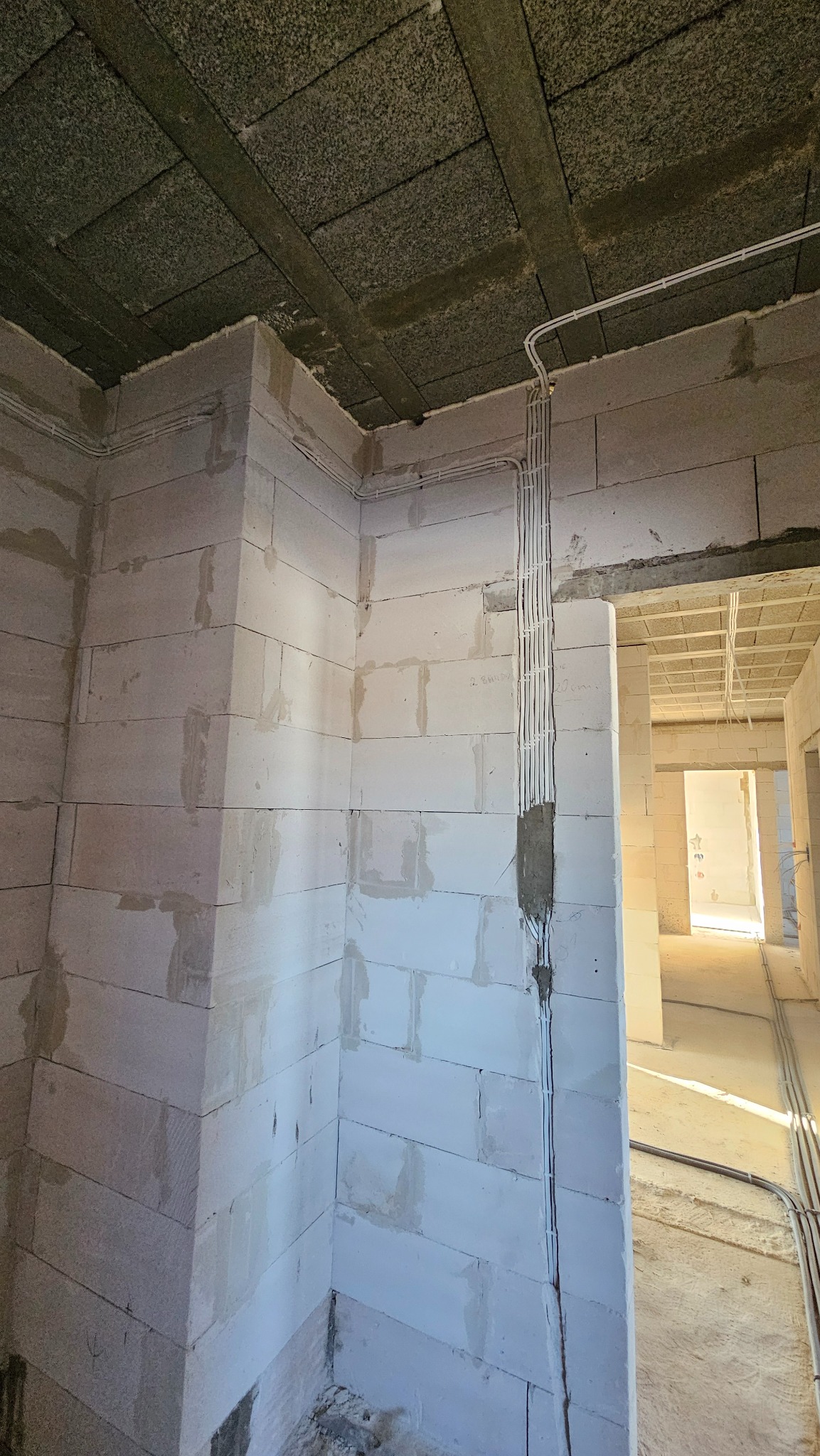 Surowy stan budynku z widocznymi przewodami elektrycznymi poprowadzonymi wzdłuż ściany z betonu komórkowego, prowadzącymi do puszki instalacyjnej.