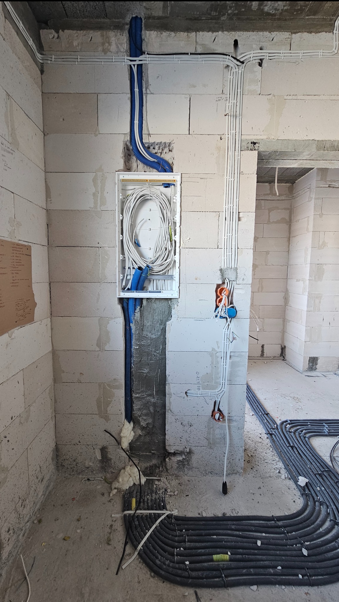 Rozprowadzenie instalacji elektrycznej w surowym stanie: białe przewody w puszce podtynkowej, niebieskie rury karbowane pionowo, czarne rury karbowane na podłodze, ściany z betonu komórkowego.
