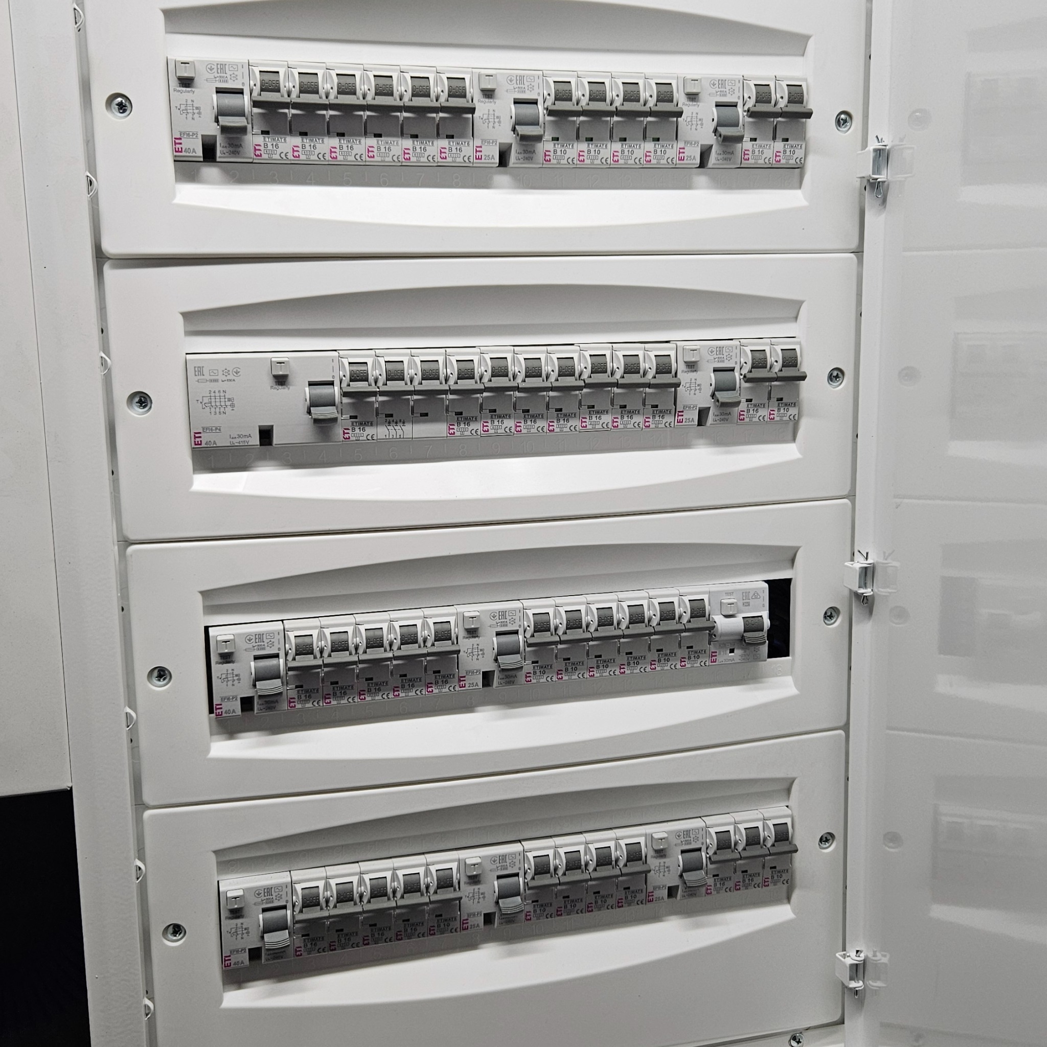 Rozdzielnica elektryczna z widocznymi bezpiecznikami i wyłącznikami, z otwartymi drzwiczkami, widok z bliska.
