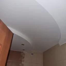 Podwieszany sufit z białej płyty gipsowej w łazience, z okrągłym obniżeniem na oświetlenie punktowe i widoczną wentylacją.