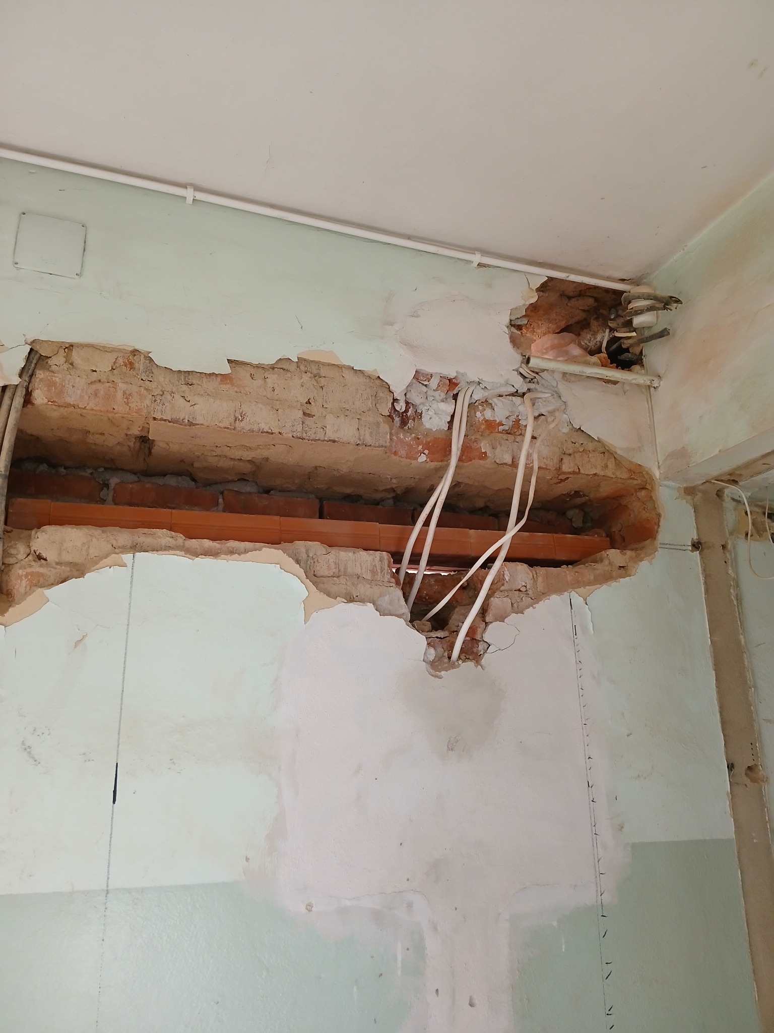 Fragment ściany z odsłoniętą konstrukcją z cegieł i instalacją elektryczną, ślady po wcześniejszych pracach wykończeniowych, widoczne przewody elektryczne.