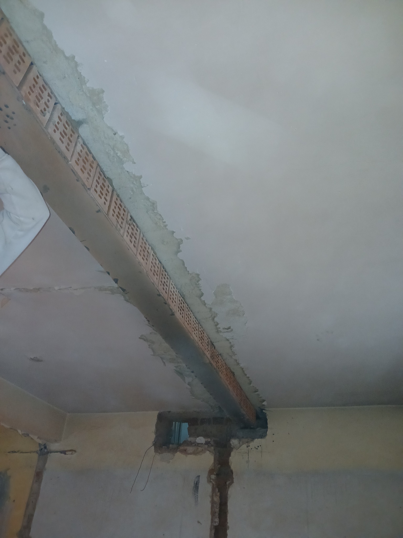 Wnętrze w trakcie remontu: widoczna konstrukcja stropu z cegieł dziurawki, surowa ściana z widocznymi instalacjami, fragment zapuszczonego okna, ślady po usuniętych płytkach lub tynku.