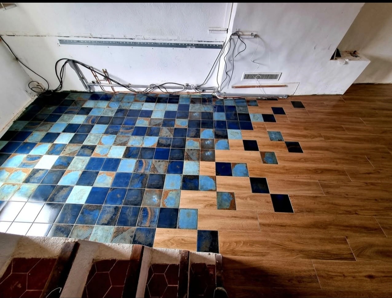 Nietypowe połączenie płytek ceramicznych w odcieniach niebieskiego z drewnopodobnymi panelami, tworzące efekt pikselizacji na podłodze w trakcie remontu.
