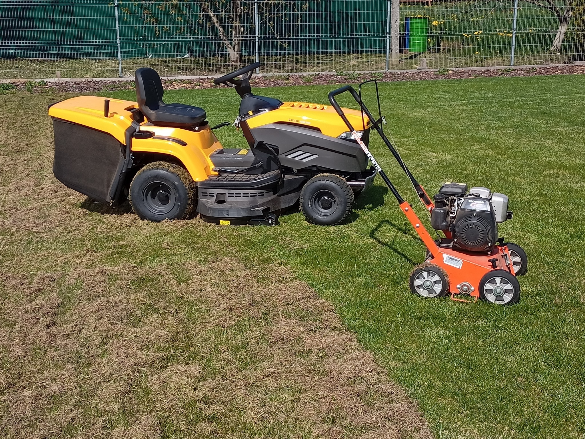 Żółty traktorek do koszenia trawy i wertykulator na trawniku, z widoczną różnicą w wyglądzie trawy po zabiegu wertykulacji.
