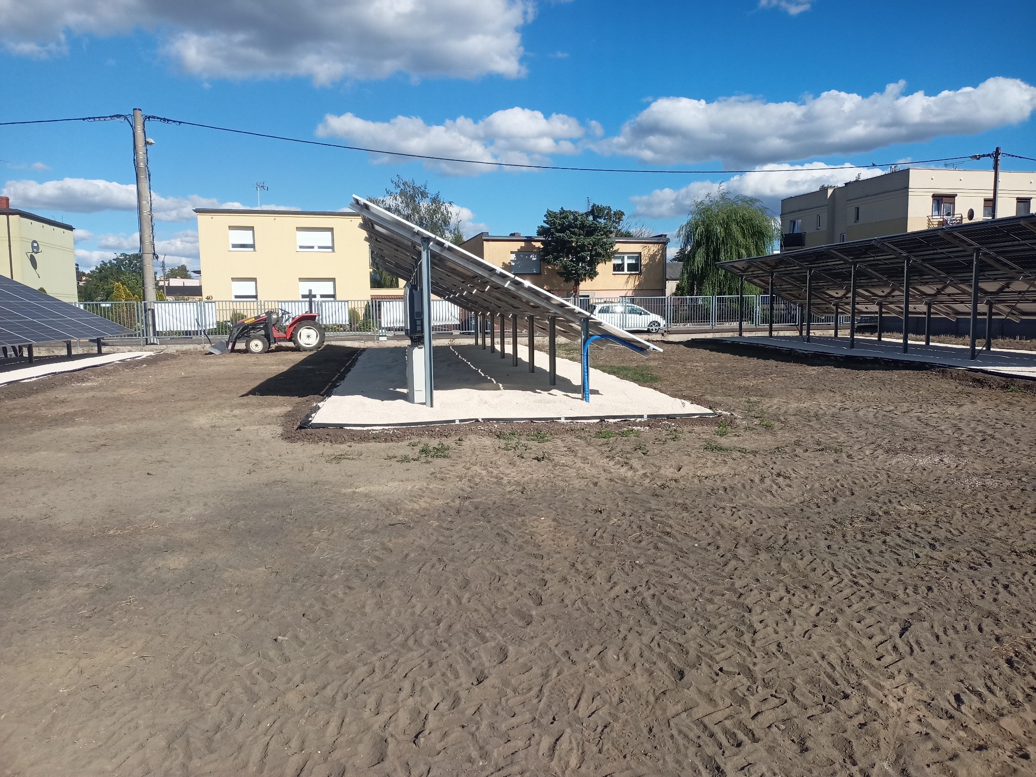 Przygotowany teren pod instalację paneli fotowoltaicznych, widoczne ślady opon i mały traktor w tle.