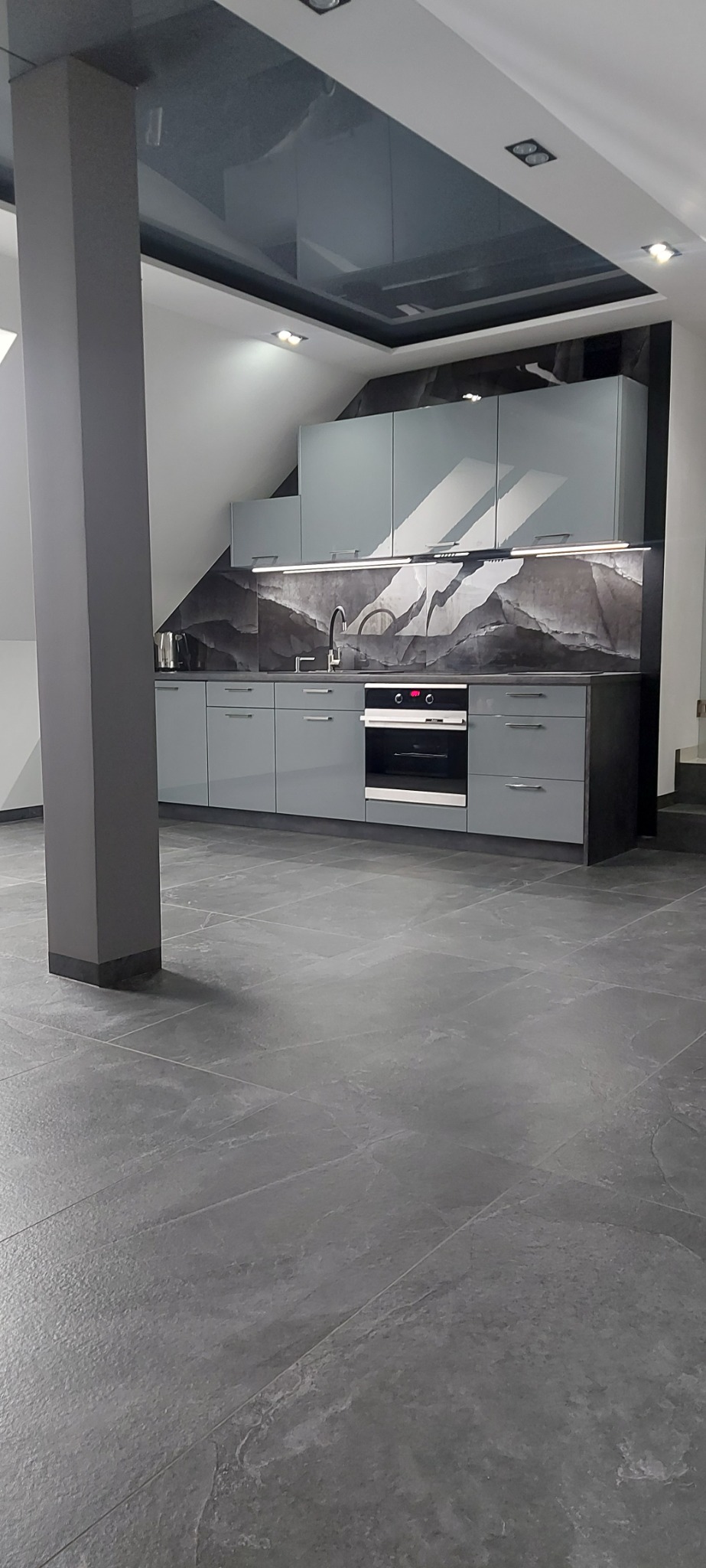 Nowoczesna kuchnia w odcieniach szarości z błyszczącym sufitem i dekoracyjnym panelem nad blatem.