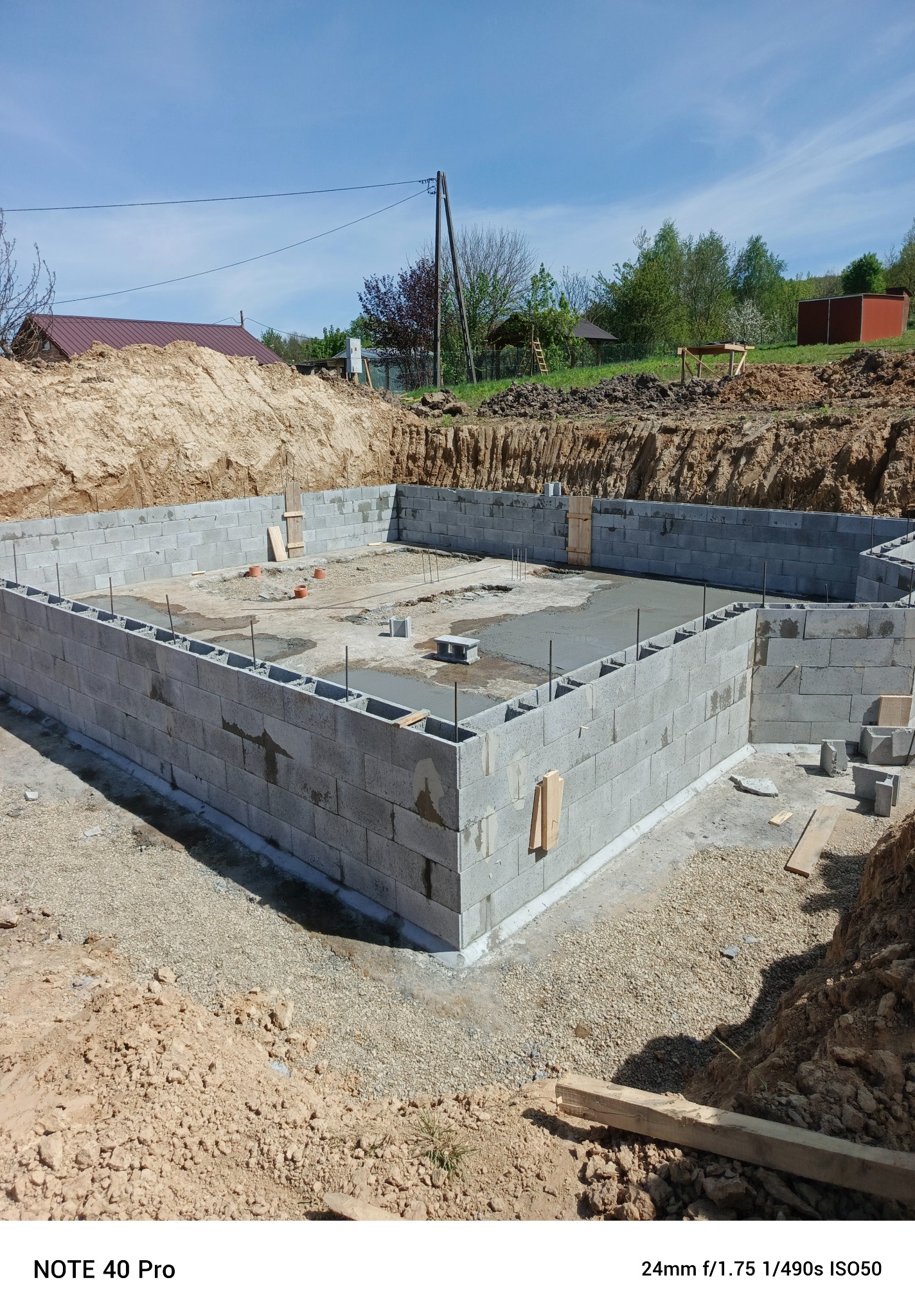 Fundamenty budynku mieszkalnego w trakcie budowy, wykonane z szarych bloczków betonowych, częściowo zalane betonem, otoczone wykopem ziemnym.