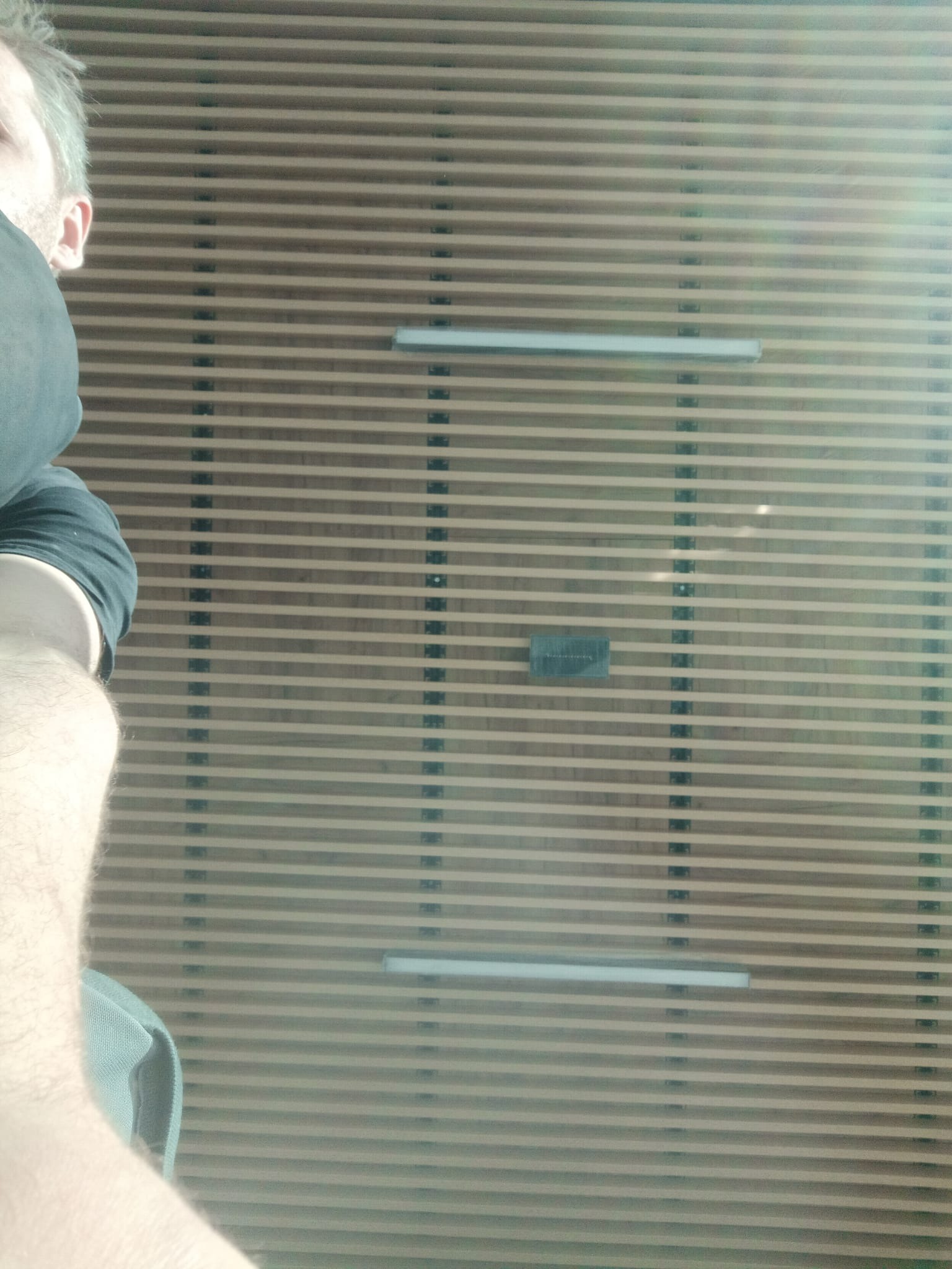 Panelowa ściana z poziomymi listwami i oświetleniem LED, widziana z perspektywy osoby stojącej blisko. Fragment ciała osoby widoczny z lewej strony.