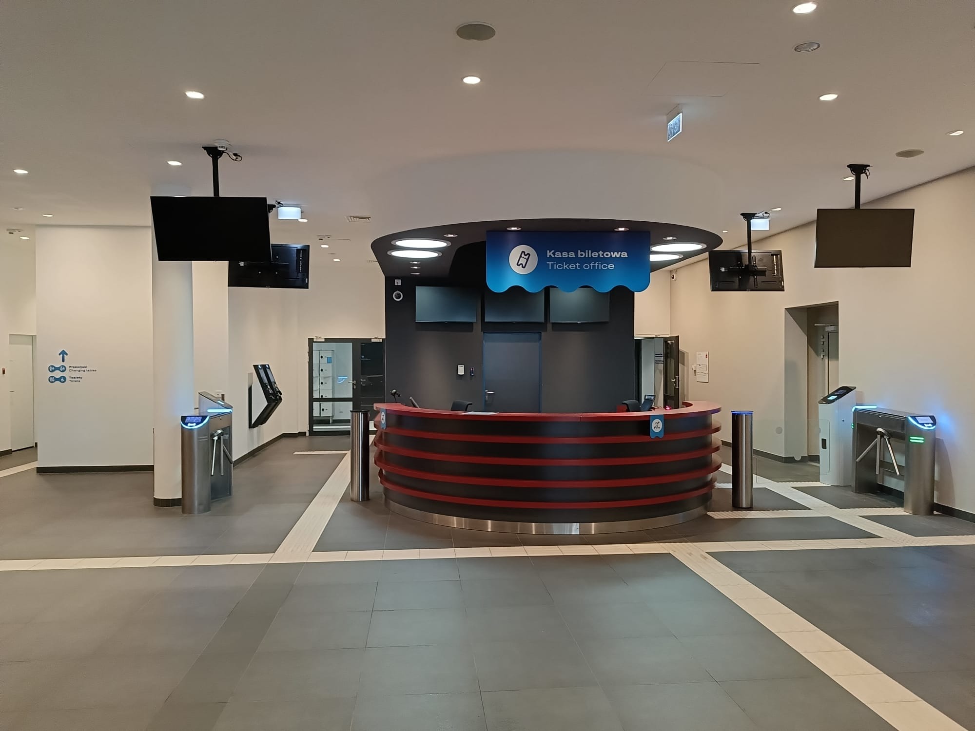 Nowoczesna kasa biletowa z kołowrotami wejściowymi w Jaworze. Widoczne ekrany LCD i oświetlenie LED. Minimalistyczny design.