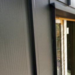 Vasil Irhovtsii - Szara, blaszana elewacja budynku z widocznym oknem w czarnej ramie. Pionowe przetłoczenia blachy. Ujęcie z dołu, podkreślające wysokość budynku.