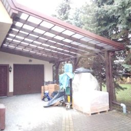 Vasil Irhovtsii - Drewniana wiata garażowa z przezroczystym zadaszeniem, przylegająca do budynku z dwoma bramami garażowymi. Częściowo zasłonięta materiałami budowlanymi.