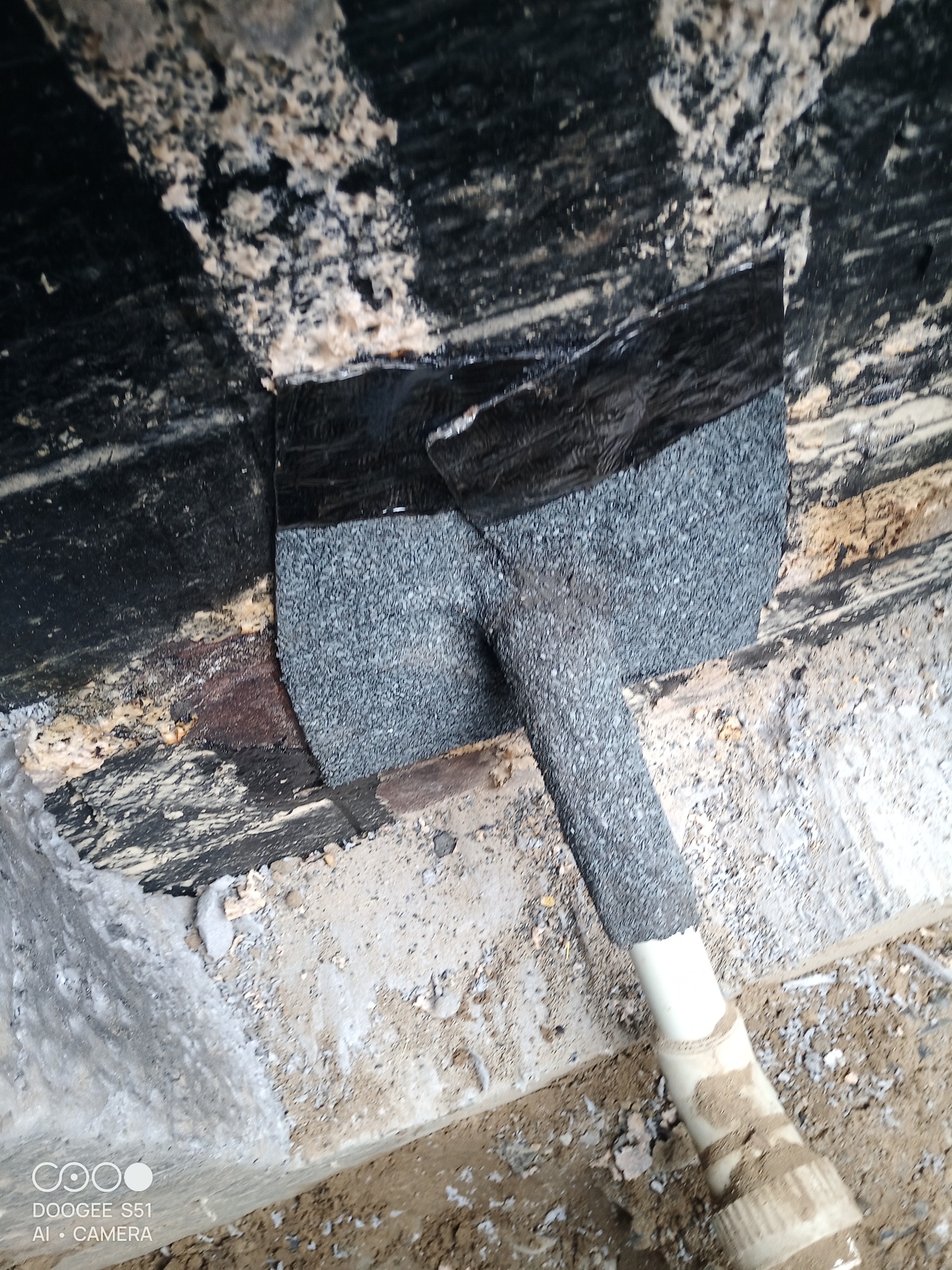 Szczegółowe ujęcie fragmentu dachu z uszczelnionym przewodem, widoczna czarna folia i szara posypka bitumiczna. Przewód z tworzywa sztucznego.