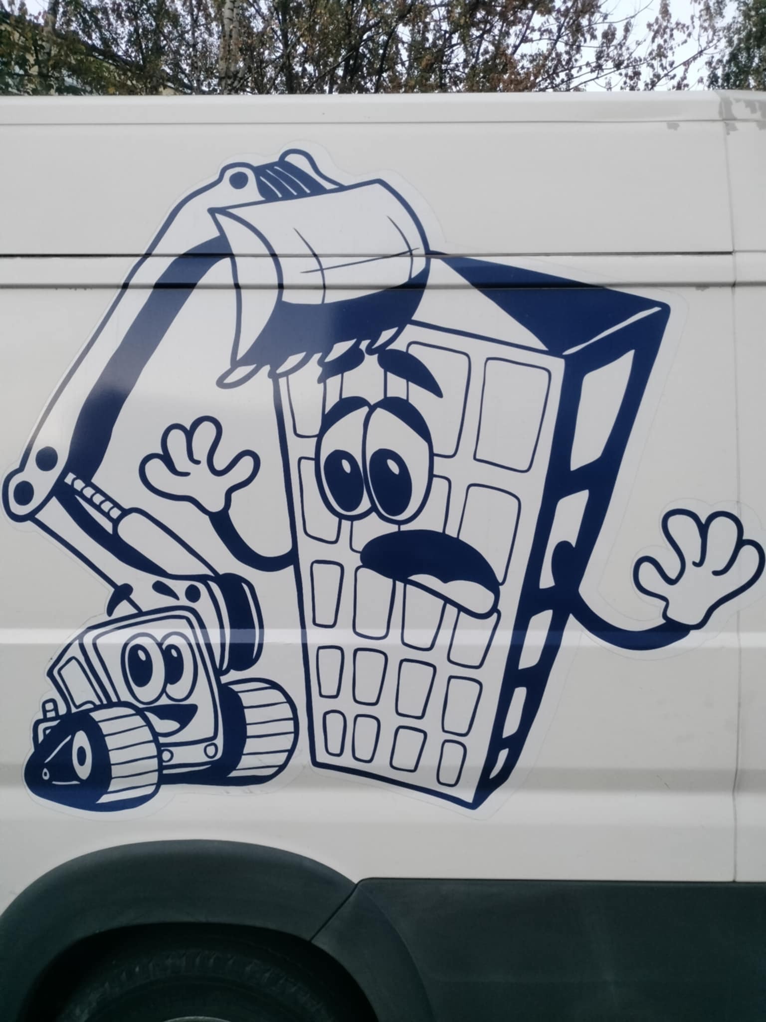 Naklejka na białym samochodzie z wesołą koparką i gruzem z oczami. Humorystyczny akcent na pojeździe firmy budowlanej.