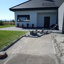 Etap układania szarej kostki brukowej na podjeździe w Kątach Wrocławskich, widoczne przygotowane elementy i narzędzia.