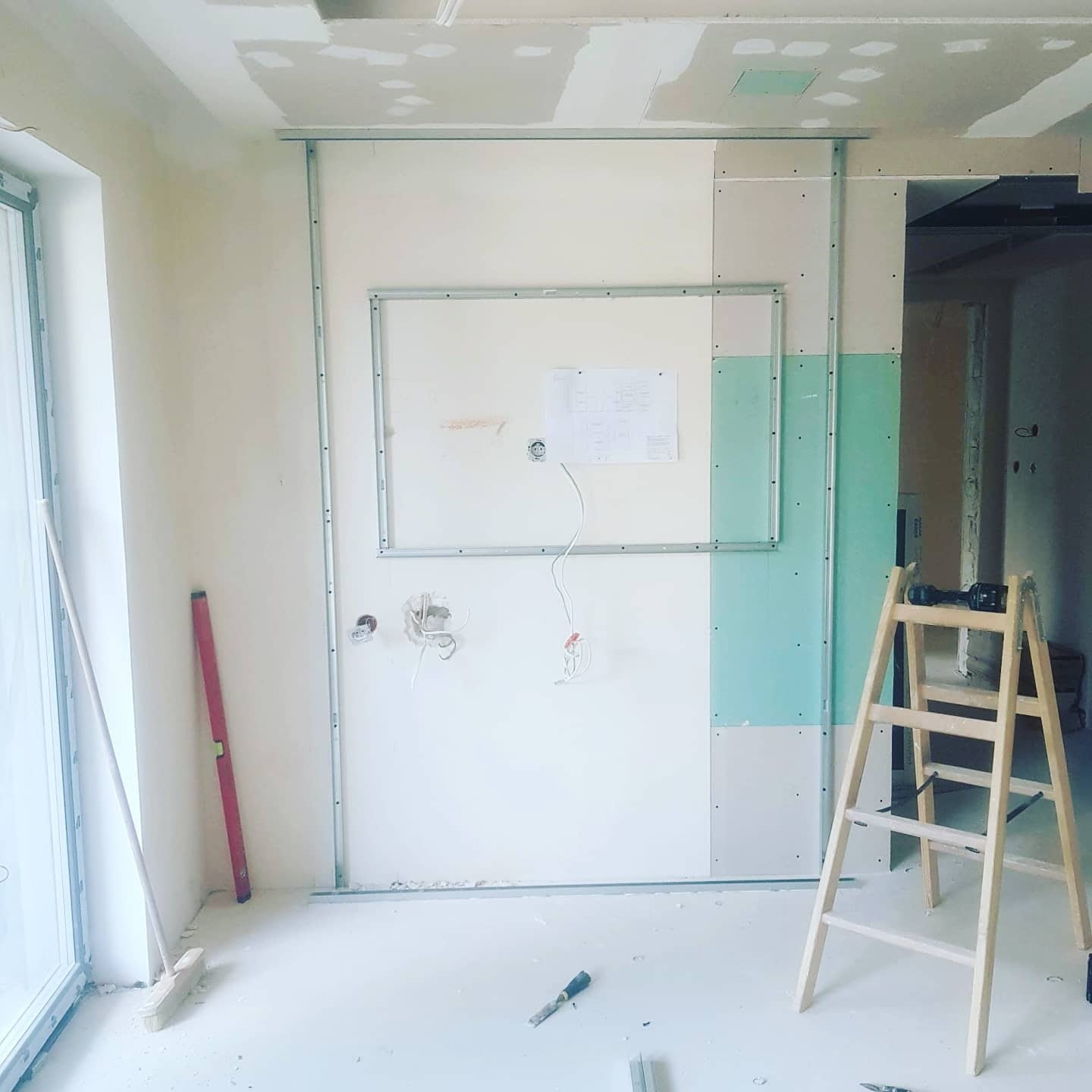 Montaż ścian działowych: metalowy stelaż, częściowo zamontowane płyty, widoczne instalacje elektryczne, drabina, poziomica i narzędzia na podłodze.