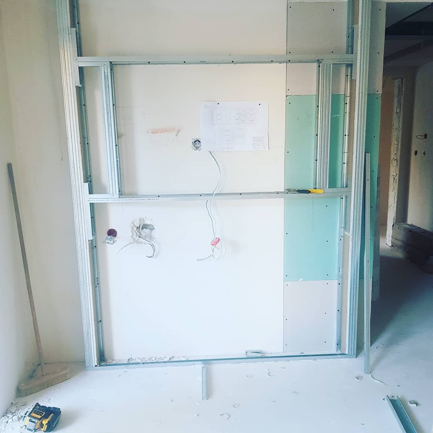 Konstrukcja metalowa pod ścianę działową z fragmentami przytwierdzonych płyt, widoczne wystające kable elektryczne i schemat na ścianie.