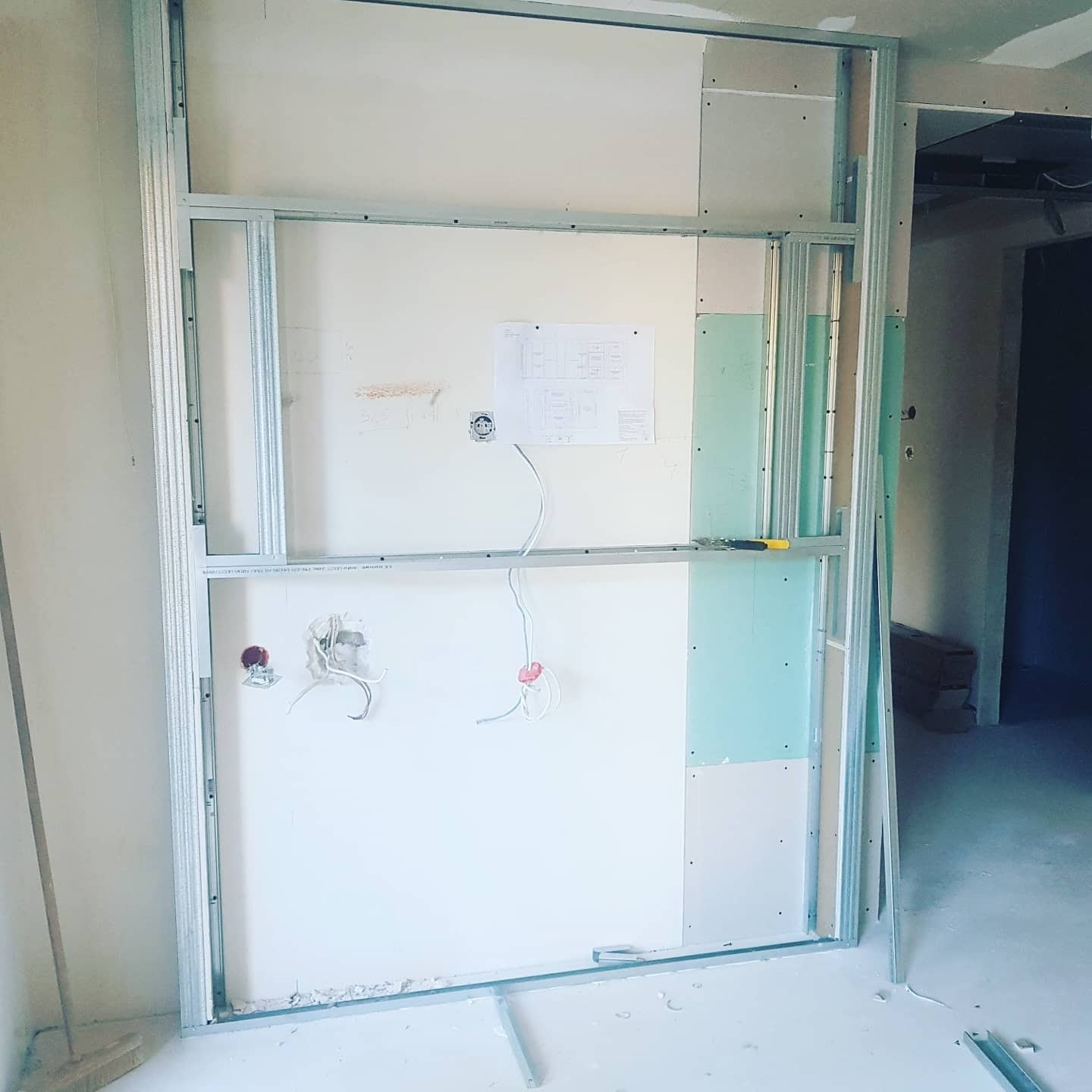 Stelaż metalowy pod płytę karton gips z widocznymi przewodami elektrycznymi i schematem instalacji, w trakcie montażu w jasnym pomieszczeniu.