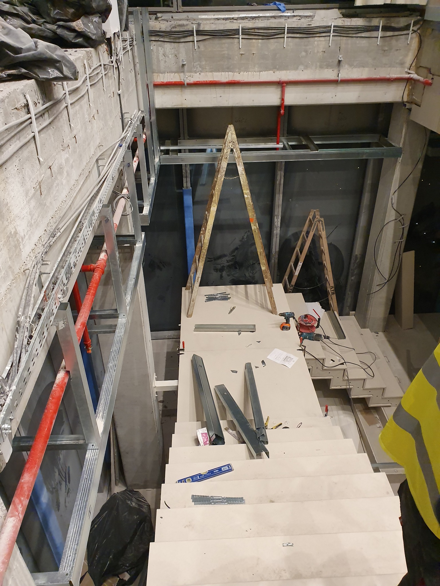 Montaż konstrukcji z profili metalowych w surowym wnętrzu budynku, widoczne drabiny, narzędzia i elementy instalacji.