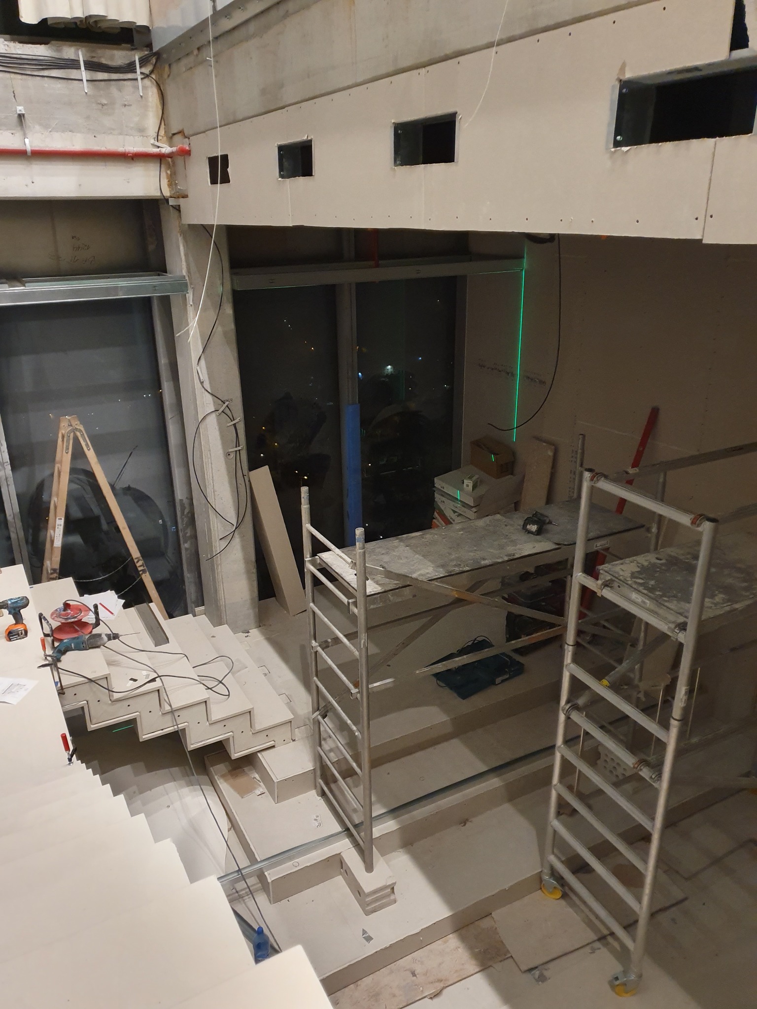 Wnętrze w trakcie prac wykończeniowych: montaż ścian działowych, widoczne rusztowania, drabina, narzędzia i zielony laser wyznaczający poziom na ścianie.
