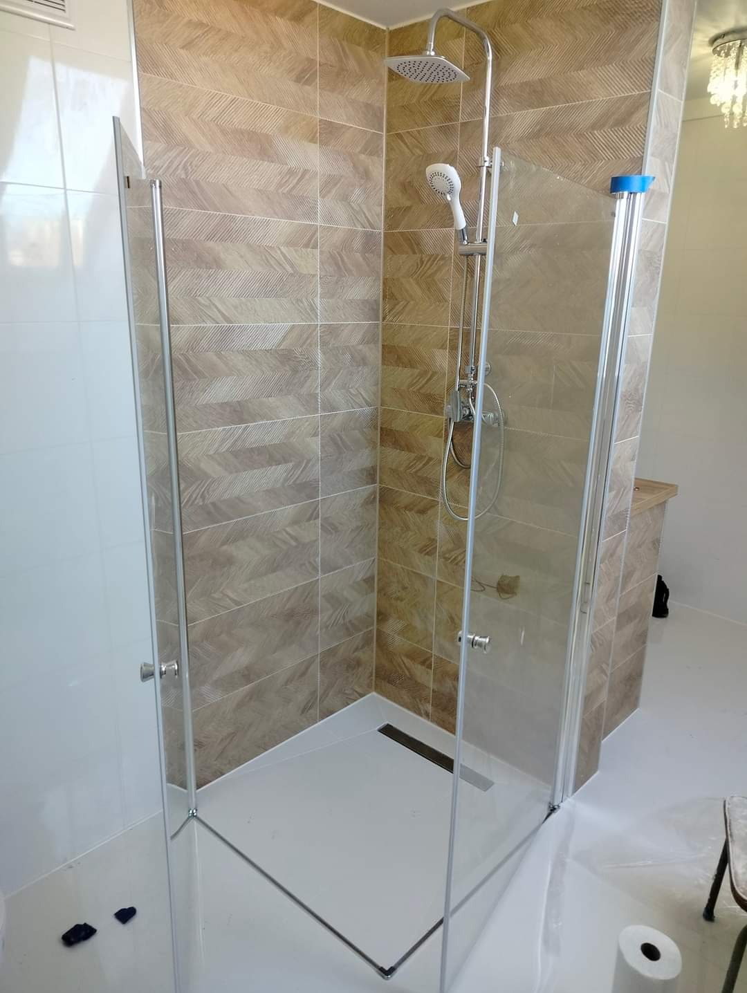 Nowoczesna kabina prysznicowa z deszczownicą i panelami ściennymi w odcieniach beżu i brązu z subtelnym wzorem chevron.