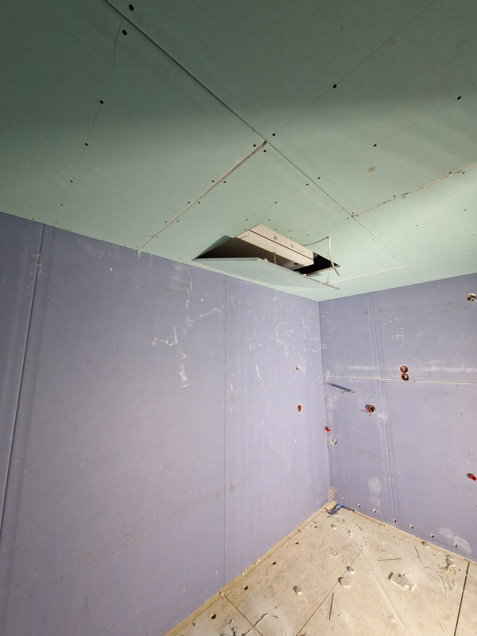 Wnętrze w trakcie prac wykończeniowych, widoczne ściany i sufit pokryte płytami gipsowo-kartonowymi, otwór rewizyjny w suficie z widoczną konstrukcją, instalacja elektryczna przygotowana do montażu...