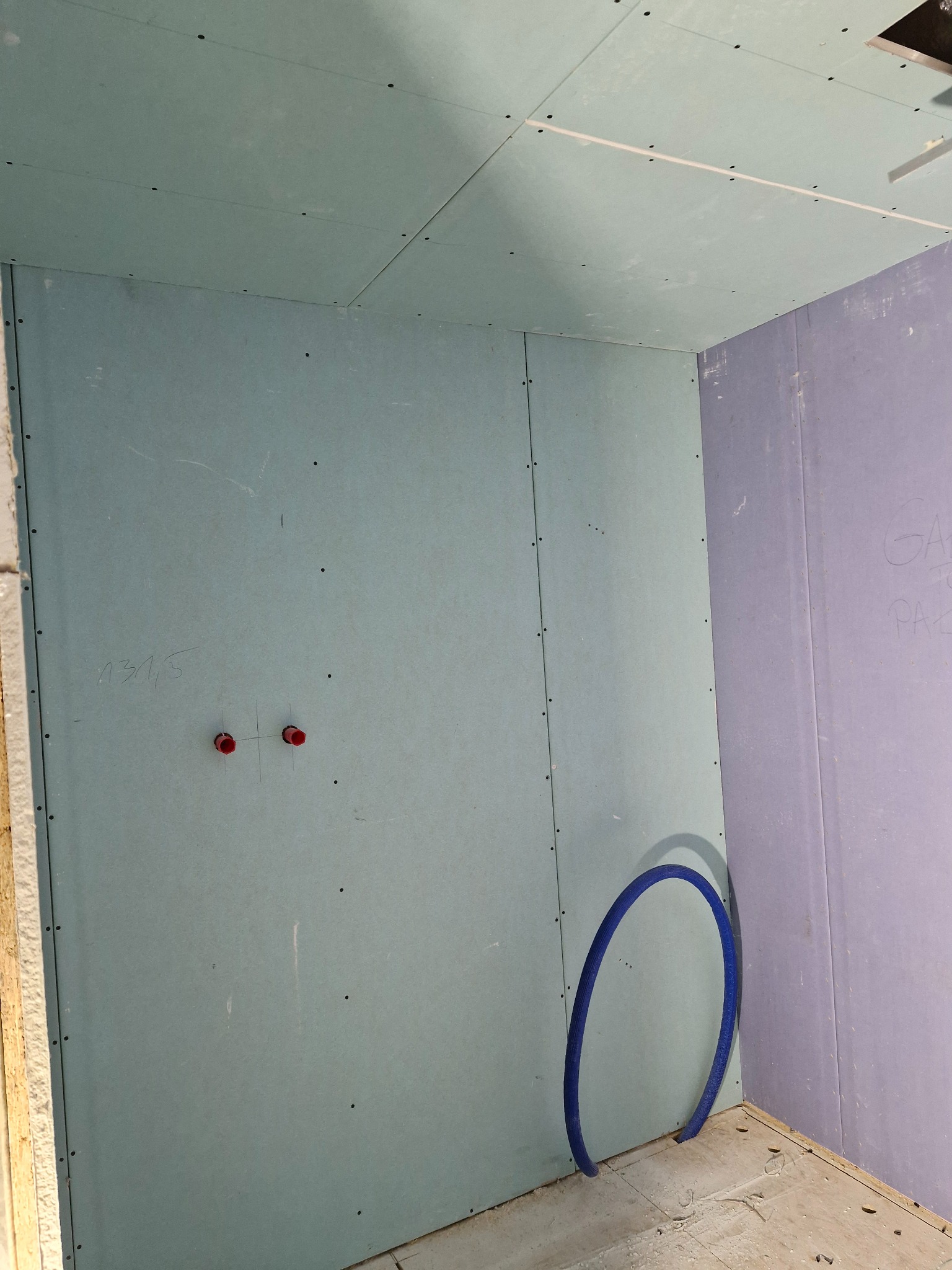 Wnętrze w trakcie montażu ścian z płyt kartonowo-gipsowych w Gdańsku, widoczne przyłącza instalacji wodnej i fragment niebieskiej rury na podłodze.