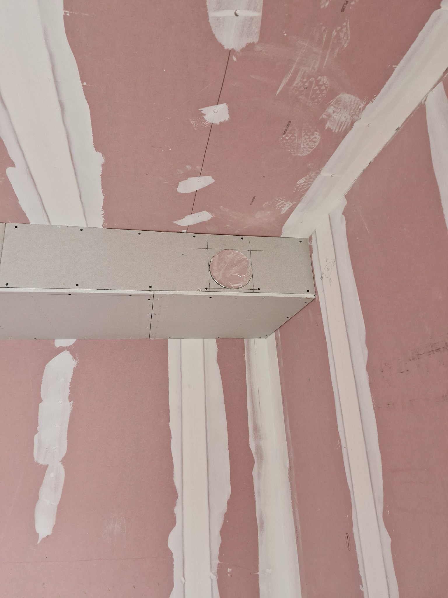 Montaż sufitu podwieszanego z płyt gipsowo-kartonowych; widoczne profile, szpachlowane łączenia, oraz otwór na instalację. Na ścianach ślady po butach i szpachli.