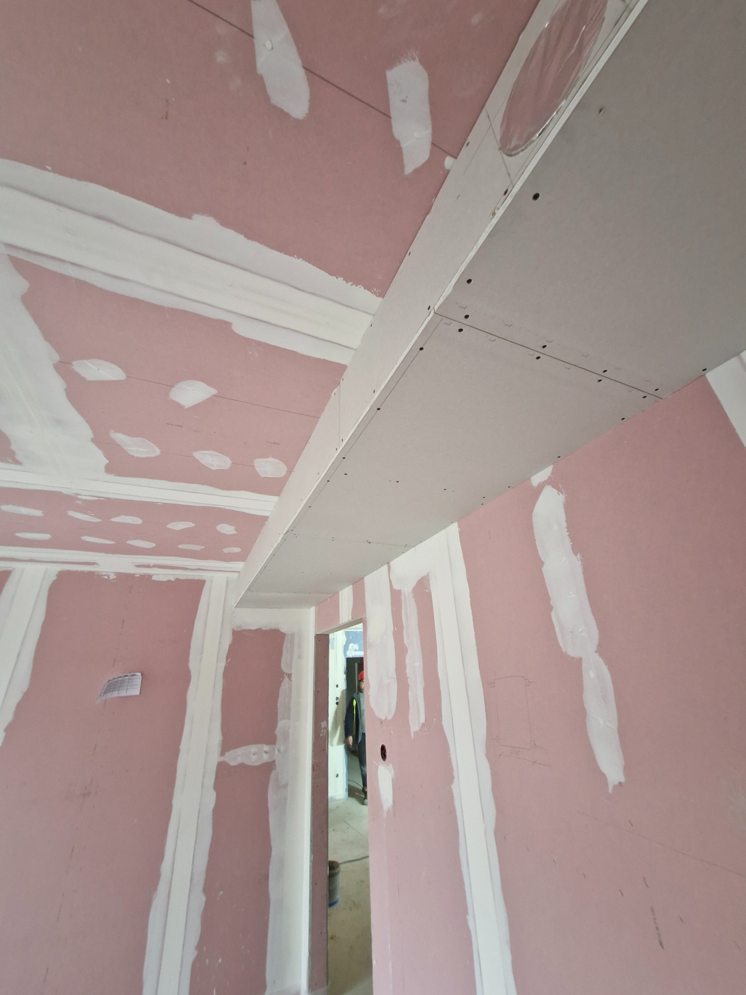 Montaż sufitu podwieszanego z płyty gipsowo-kartonowej, widoczne łączenia płyt i szpachlowanie, różowe ściany w tle.