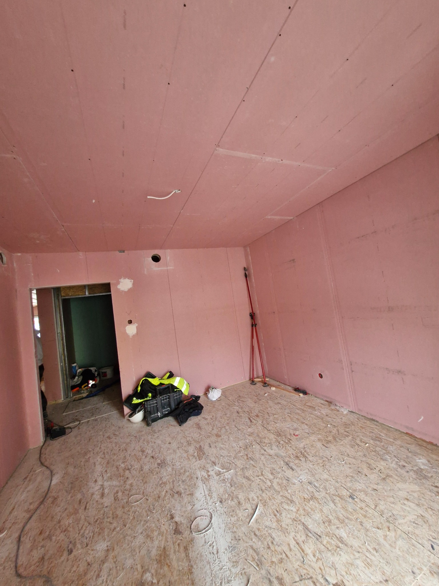 Pokój w trakcie remontu z zamontowanymi różowymi płytami na ścianach i suficie, widoczne narzędzia i akcesoria budowlane na podłodze.