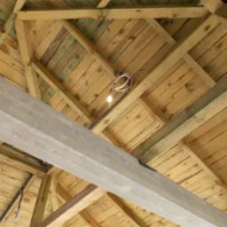 Drewniany strop z widoczną instalacją oświetleniową i betonową belką, widok z dołu, surowe wykończenie, jasne drewno, kabel z żarówką.