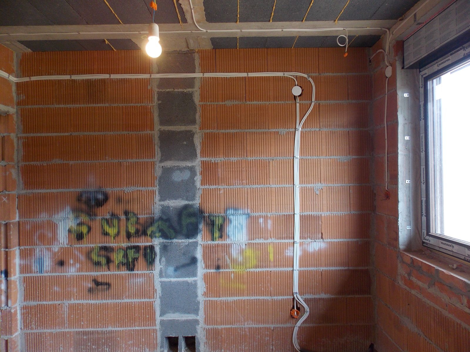 Instalacja elektryczna w surowym budynku we Wrocławiu. Widoczne kable poprowadzone po ceglanej ścianie i pod sufitem. Żarówka na kablu oświetla wnętrze.