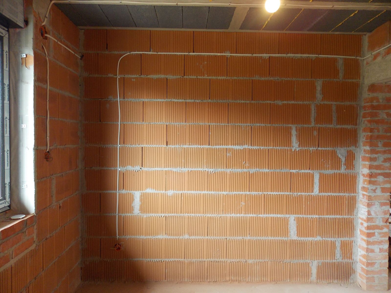 Wnętrze w trakcie prac: instalacja elektryczna natynkowa, kable prowadzone wzdłuż ceglanej ściany, widoczne puszki instalacyjne, surowy stan wykończenia.