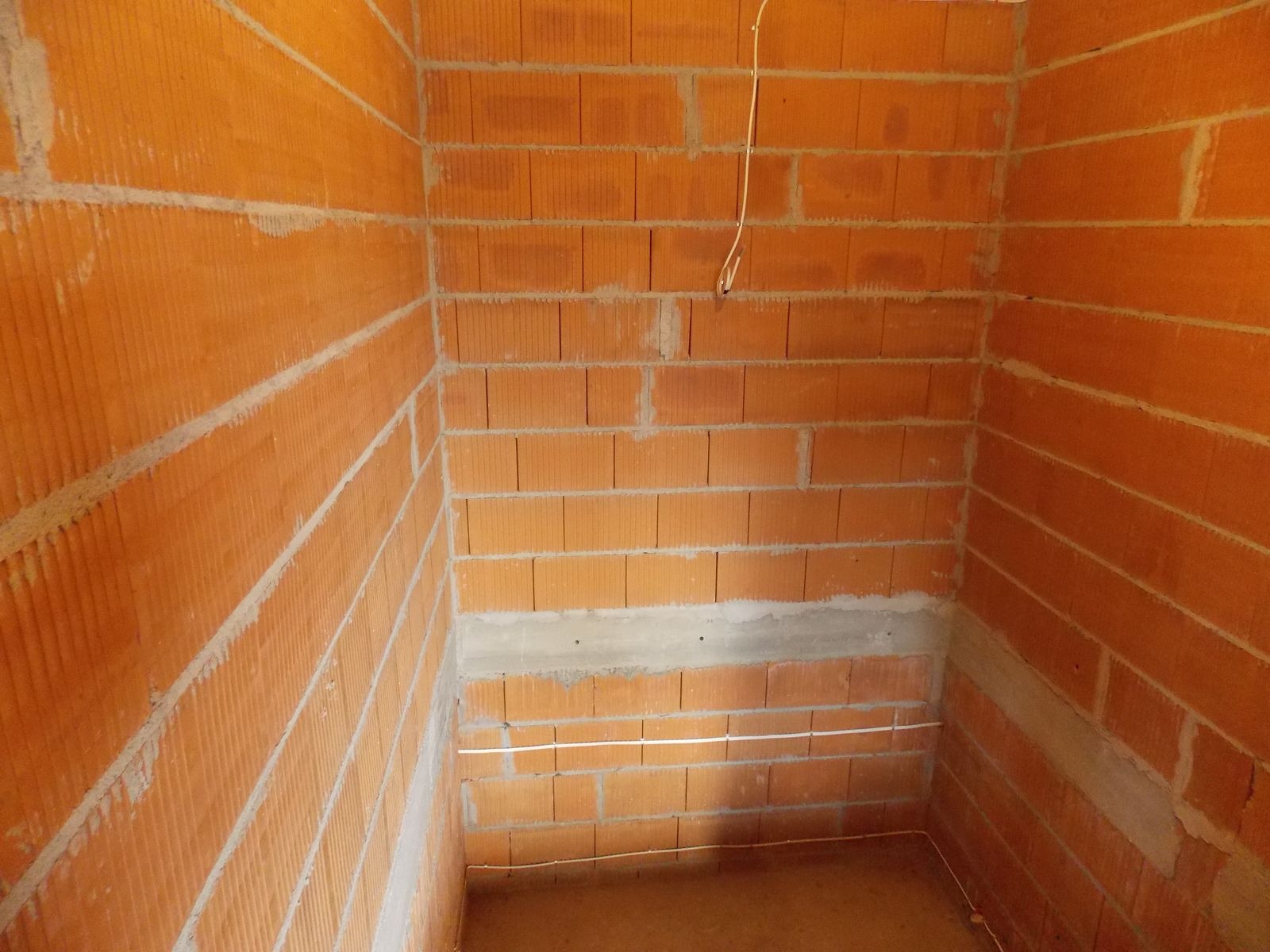 Surowy mur z cegły dziurawki w trakcie prac instalacyjnych. Widoczne przewody elektryczne ułożone wzdłuż ścian. Ściany w stanie deweloperskim.