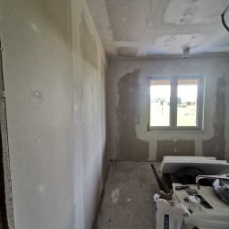 Przemysław Filipiak - Pokój w trakcie remontu, ściany i sufit częściowo pokryte gładzią szpachlową, widoczne narzędzia i worek z gładzią Uniflott na podłodze.