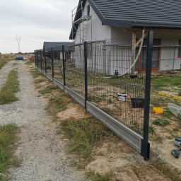 Przemysław Filipiak - Montaż panelowego ogrodzenia z podmurówką betonową, widoczne narzędzia i materiały budowlane, dom w tle w trakcie prac wykończeniowych.