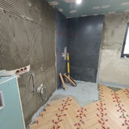 Przemysław Filipiak - Wnętrze w trakcie prac wykończeniowych: układanie parkietu w jodełkę z użyciem klipsów, ściana z nałożonym klejem do płytek i fragment wykończonej ściany z ciemnych płytek.