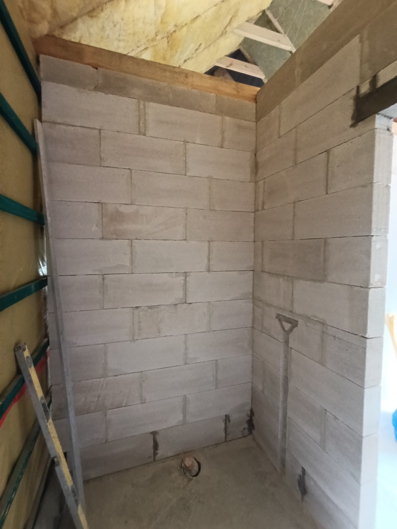 Wnętrze w trakcie budowy z bloczków, widoczne ocieplenie stropu i poziomica oparta o ścianę. Surowy stan, przygotowanie do dalszych prac wykończeniowych.