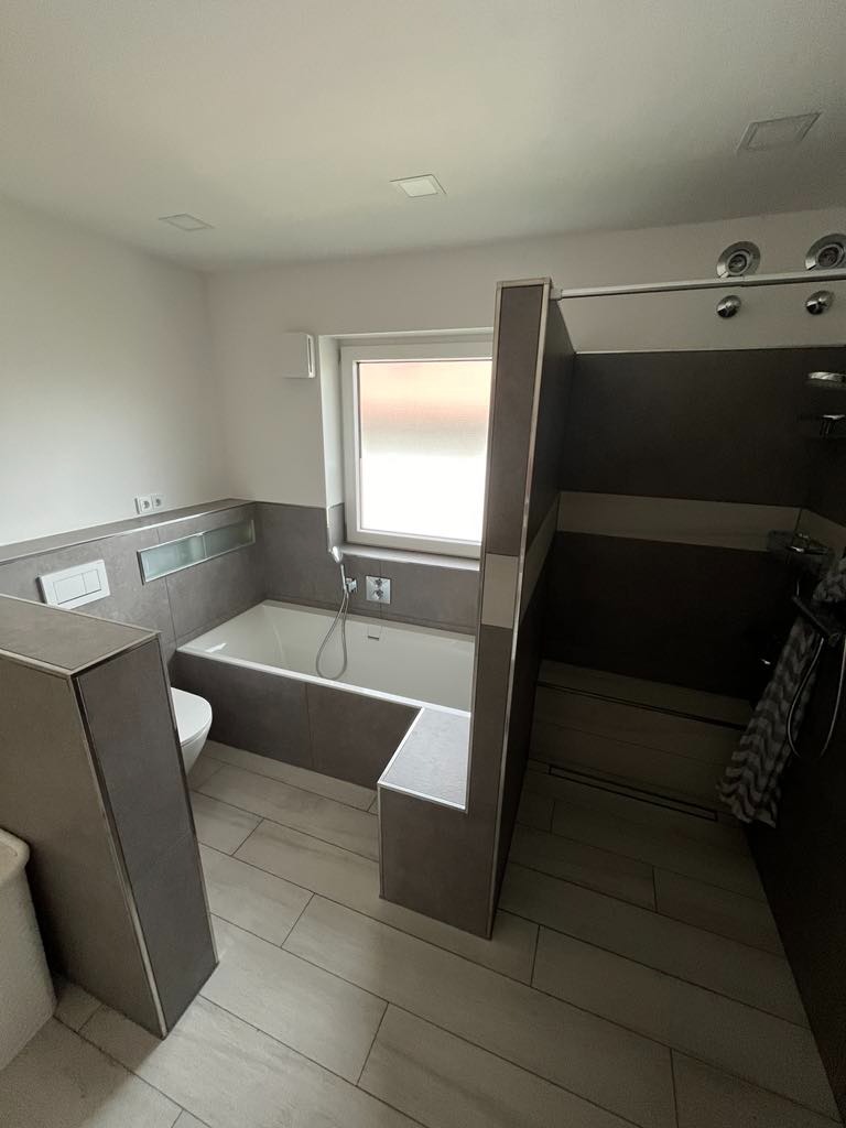 Nowoczesna łazienka w odcieniach szarości z wanną, kabiną prysznicową typu walk-in i płytkami imitującymi drewno na podłodze.