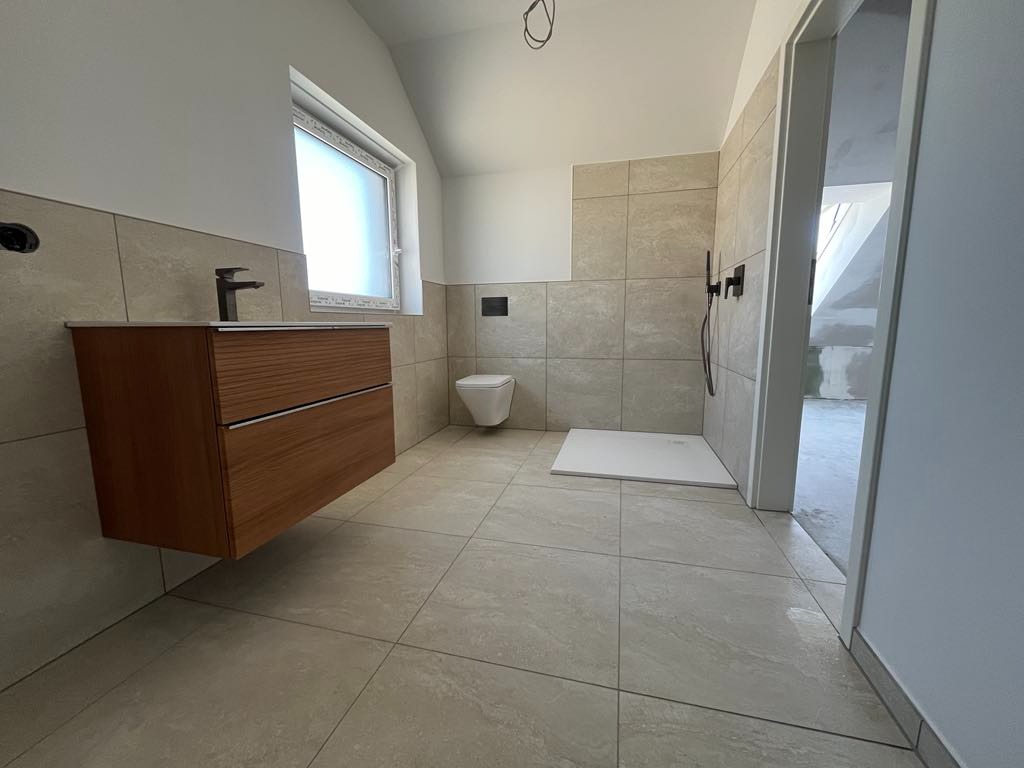 Wykończona łazienka w beżowych płytkach z wiszącą szafką z umywalką, toaletą i brodzikiem bez kabiny.