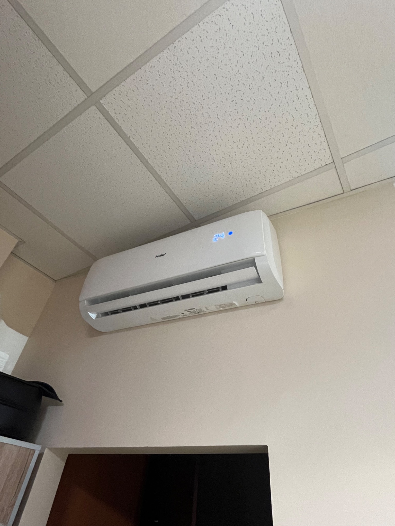 Biała klimatyzacja Haier zamontowana na ścianie w pomieszczeniu z kasetonowym sufitem, ustawiona na 24 stopnie Celsjusza.