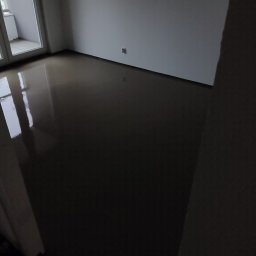 PatPanele Patryk Ninard - Świeżo wylana, ciemna posadzka w pomieszczeniu z balkonem, widoczne odbicia światła w gładkiej powierzchni.